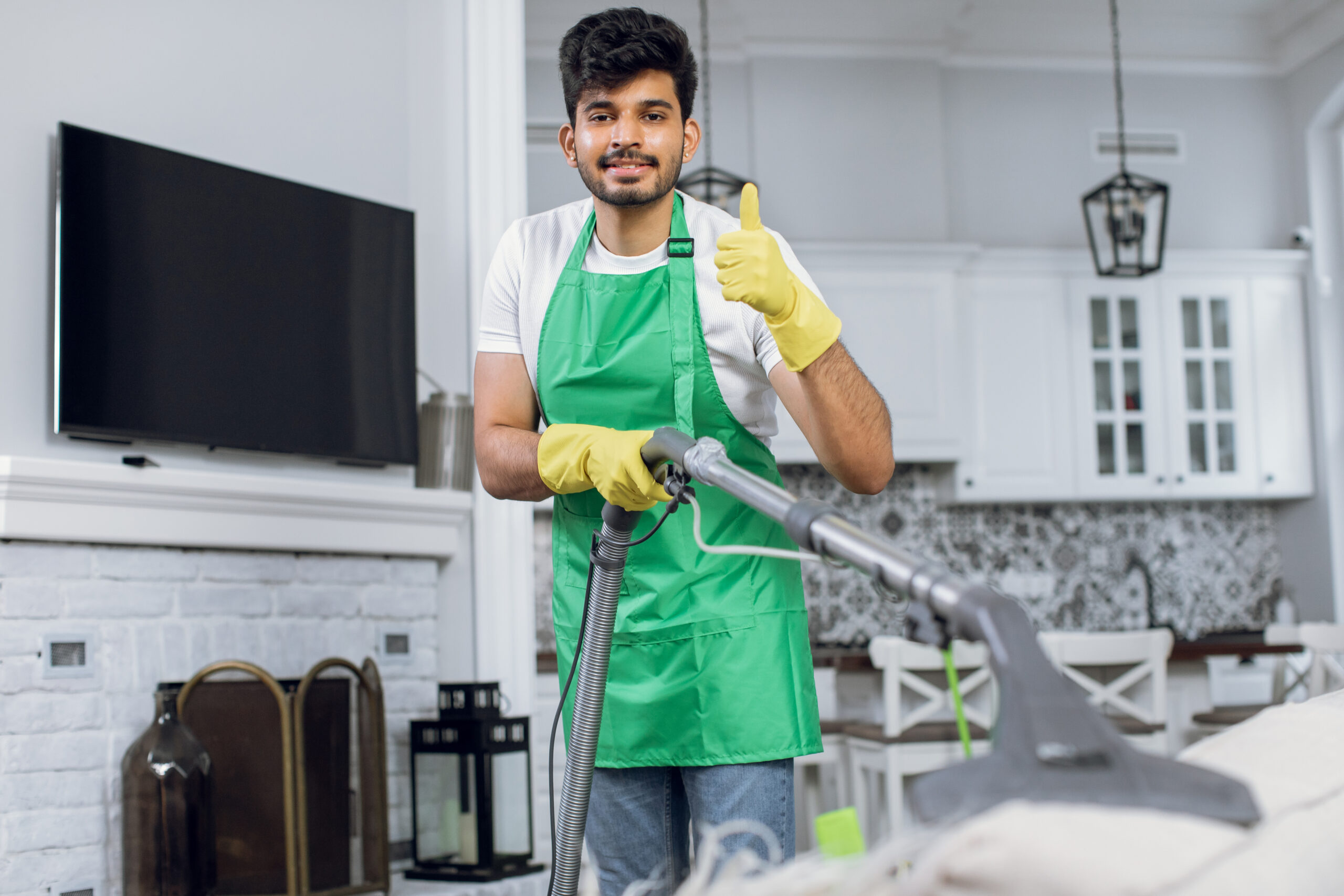 indian guy showing thumb up while cleaning couch with vacuum